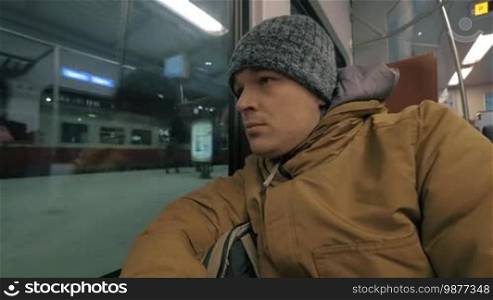 Man in winter overclothes looking out the window during his everyday ride in commuter train