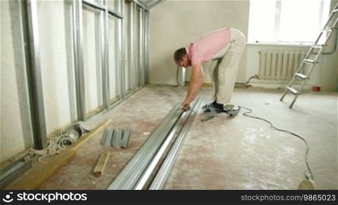 Man installing plasterboard walls in the house, measuring the size of drywall studs