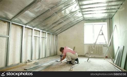 Man installing plasterboard walls in the house, working with a screw gun