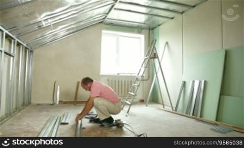 Man installing plasterboard walls in the house, working with a screw gun