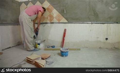 Man installs ceramic tile - mixing grout, Wide Angle, Rear View