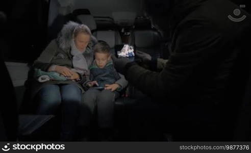 Man making mobile video of mother and son traveling by minibus in winter evening, child playing on cellphone
