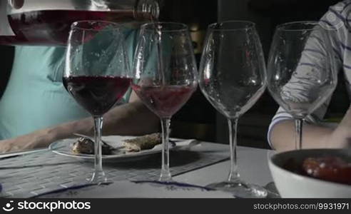 Man pouring red wine in four glasses. Unrecognizable