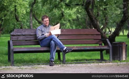 Man reads a newspaper on a bench in the park