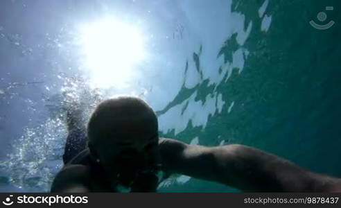 Man swimming underwater, free diving and holding GoPro video camera. Leisure, summer fun, recreation, holiday, vacations, water sport in Mediterranean Sea, Italy