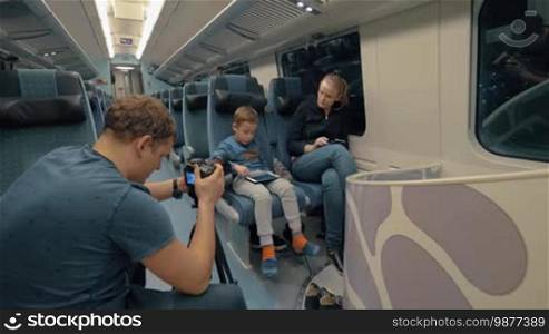 Man takes footage of a mother and son traveling on an express train, passing time with a tablet and cellphone