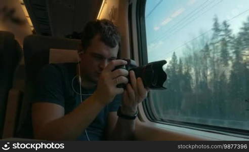 Man traveler listening to music and shooting outside scenes with camera when traveling by train