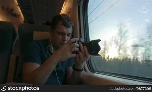Man traveling in express train. He listening to music in earphones and shooting video of outside scenes at sunset. Then he looking out the window