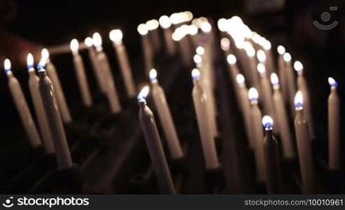 Many candles are burning on a candlestick, on the left side a hand takes another candle and lights it