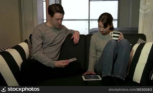 Married people, marriage relationship, white husband and Asian wife at home. Man reading newspaper and Japanese woman using iPad digital tablet. Interracial couple fun, lifestyle and technology