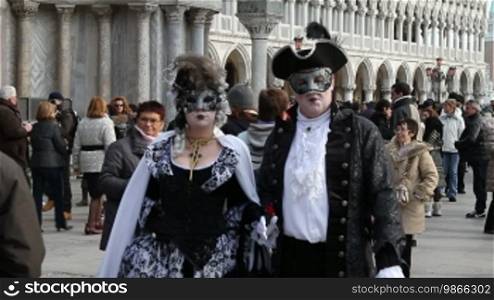 Masked couple and tourists, on St. Mark's Square, in Venice.
