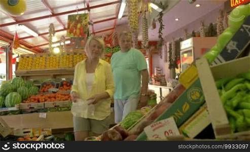 Mature family couple taking ripe and sweet peaches and putting them into packet. Shopping in market with great assortment of fresh fruit and vegetables