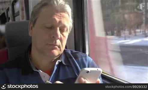 Mature man is writing messages in smartphone while traveling by train.