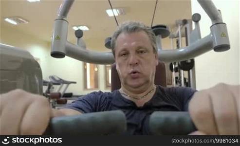Mature man working out on exercising machine in a gym. Training chest muscles. Healthy way of life