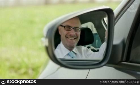 Mid adult Caucasian business man looking at camera through rear view mirror. Dolly shot