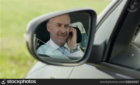 Mid adult Caucasian business man talking on the phone, viewed from the rear view mirror.