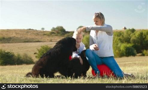 Mother and daughter having fun with their Newfoundland dogs in nature