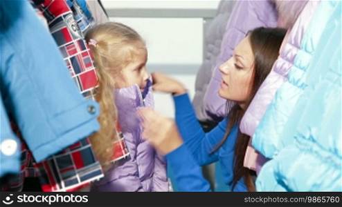 Mother and daughter shopping for clothes in a clothing store, trying on winter coat