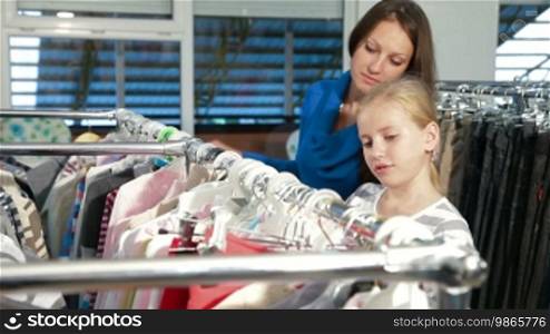 Mother and daughter shopping for girls clothes in a clothing store, looking at sweaters. Side view