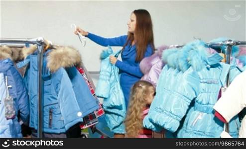Mother and daughter shopping for winter clothes in a clothing store, looking at down-padded coat