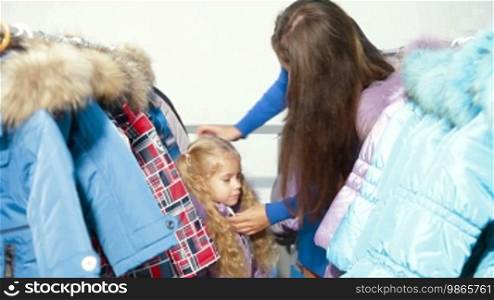 Mother and daughter shopping for winter clothes in a clothing store, trying on down-padded coat