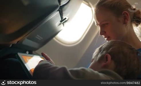 Mother and her little son playing game on touchpad in the plane