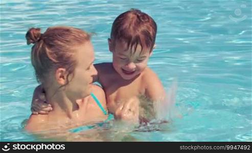 Mother and her little son with floating ring swimming in rough water of the pool. Smiling, kissing, laughing and hugging.