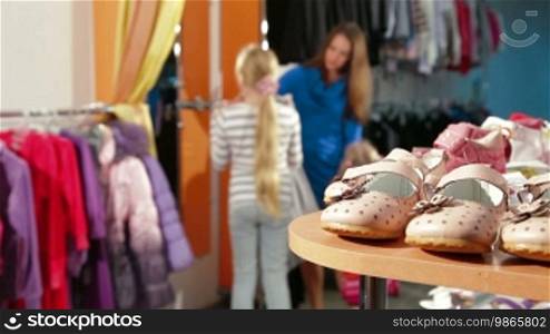Mother and little daughter shopping for girls' clothes in a clothing store, focus on the foreground