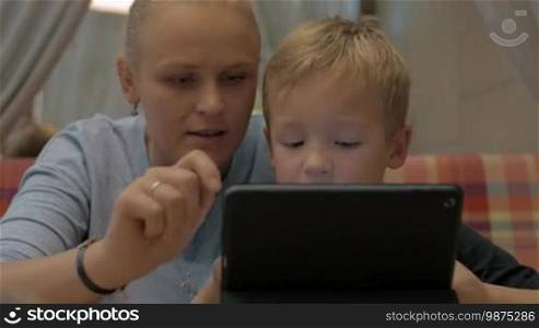 Mother and son spending time in cafe with tablet computer. Woman educating child by means of touch pad