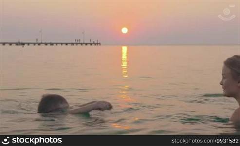 Mother and son swimming in the sea at sunset. Boy learning to dive under mom's supervision, she encouraging and kissing kid