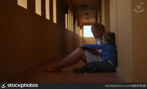 Mother and son with a book sitting on the floor of hotel hall. Mom teaching her little child