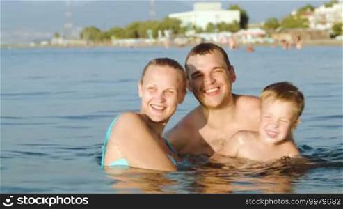 Mother, father, and son bathing in the sea at a resort on a hot day. They are having fun splashing water together. Family summer vacation