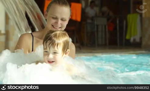 Mother holding her little son having fun in the boiling water of the pool