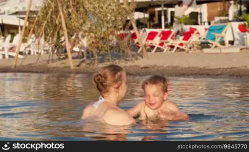 Mother playing with her young son tossing him up in the beach waters on a sunny day during holidays