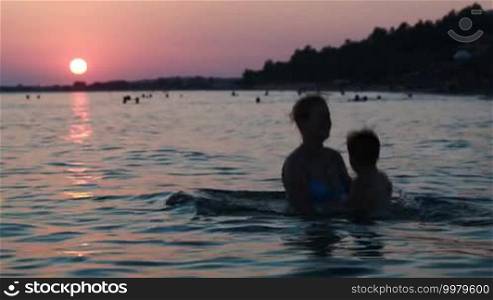 Mother playing with little son in sea water at sunset throwing him up