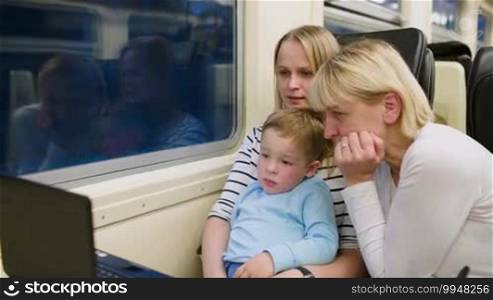 Mother, son, and grandmother watching video on laptop in the train