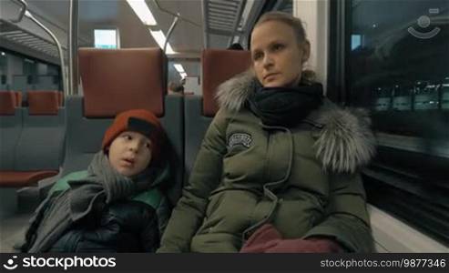 Mother talking to son while they are traveling by suburban train in winter evening