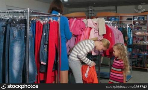 Mother with two daughters shopping for clothes in a clothing store, choosing children's jacket