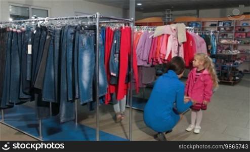 Mother with two daughters shopping for clothes in a clothing store, choosing children's jacket