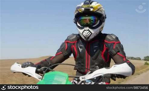 Motocross racer in motorcycle gear riding bike on rural road medium shot front view