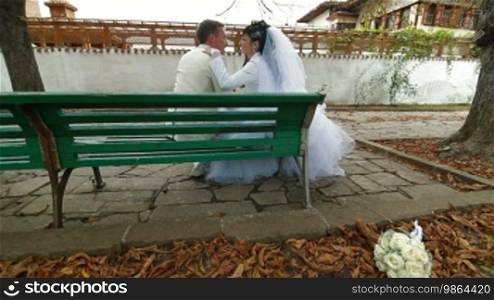 Newlyweds embracing on a bench in autumn park