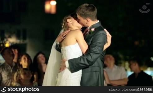 Newlyweds kissing at night, surrounded by visitors and relatives