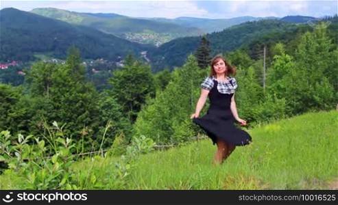 Nice happy woman dances on grass among beautiful mountains