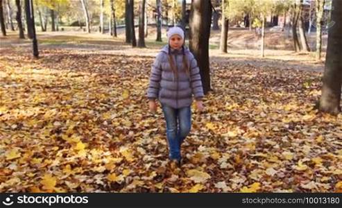 Nice teen girl goes on yellow leaves in beautiful autumn city park, slow motion
