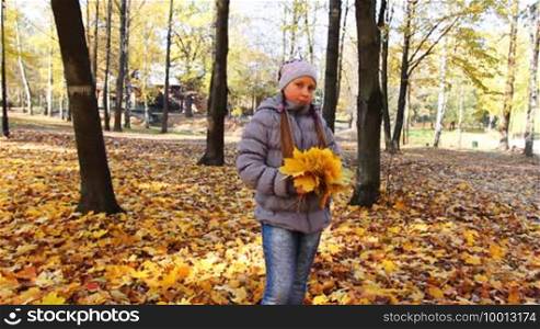 Nice teen girl stands with yellow leaves in beautiful autumn city park, then tosses it up and goes away