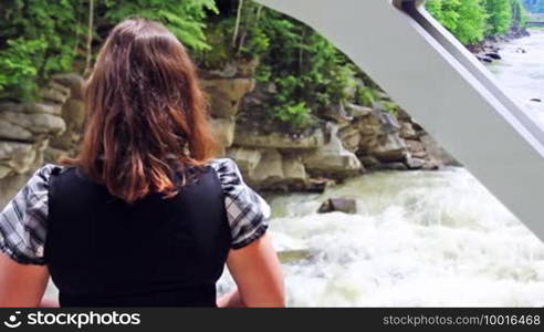 Nice woman stands back and looks at Yaremcha waterfall under the bridge