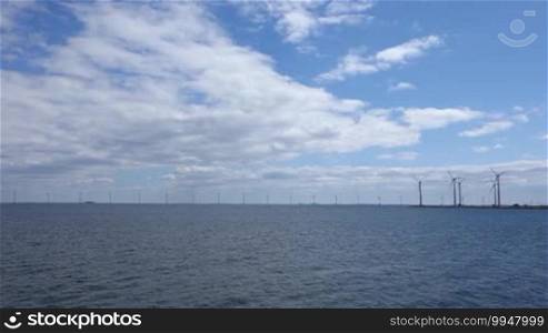 Off-Shore Wind turbines in the sea with waves under a blue sky