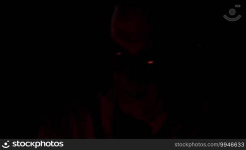 Old man in glasses sitting in the darkness with fire enlightening his face.