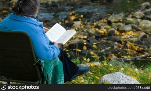 Old woman reading a book in an autumn park covered with a blanket