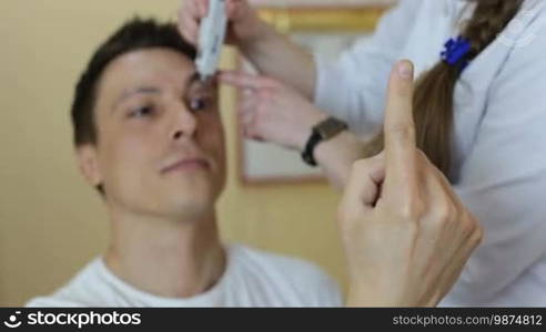 Ophthalmologist measuring intraocular pressure of male patient with handle tonomoter in ophthalmology clinic. Experienced female optometrist with handle tonometer checking patient intraocular pressure in oculist office.